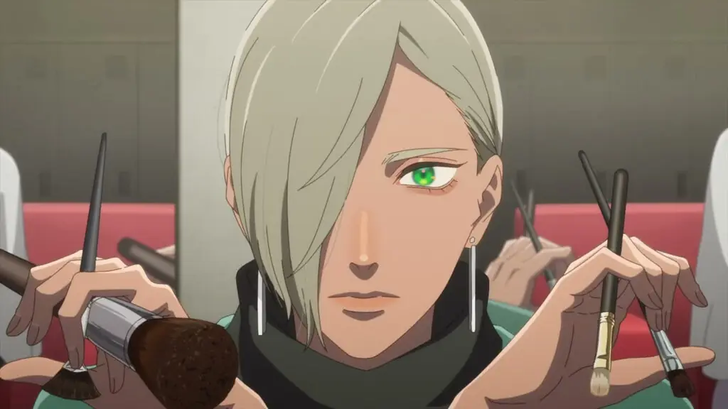 Personaje de pelo claro y ojos verdes con aros largos que sostiene varias brochas de maquillaje, en un fotograma del video promocional del anime