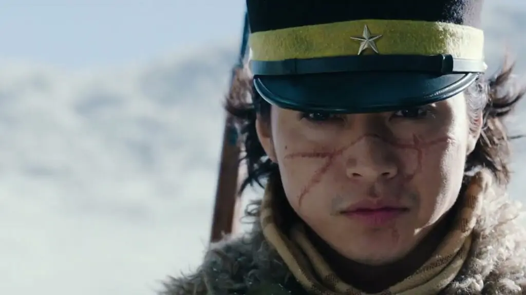Fotograma del avance: primer plano de un joven con gorra militar con estrella, cicatrices en el rostro, abrigo de piel y bufanda, sobre un paisaje nevado