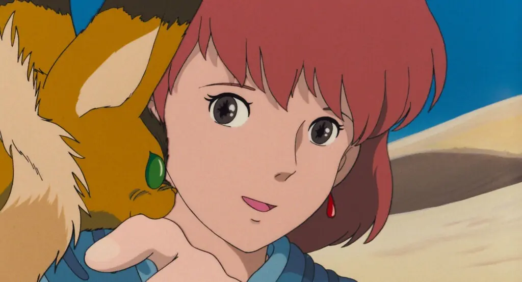 Fotograma de la película Nausicaä del Valle del Viento: la protagonista de pelo corto mira de lado, con una criatura de pelaje dorado sobre el hombro, frente a las dunas