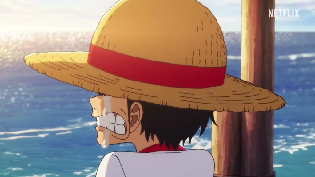 Fotograma del avance oficial de The One Piece: un joven con sombrero de paja, con una lágrima y los dientes apretados, frente al mar